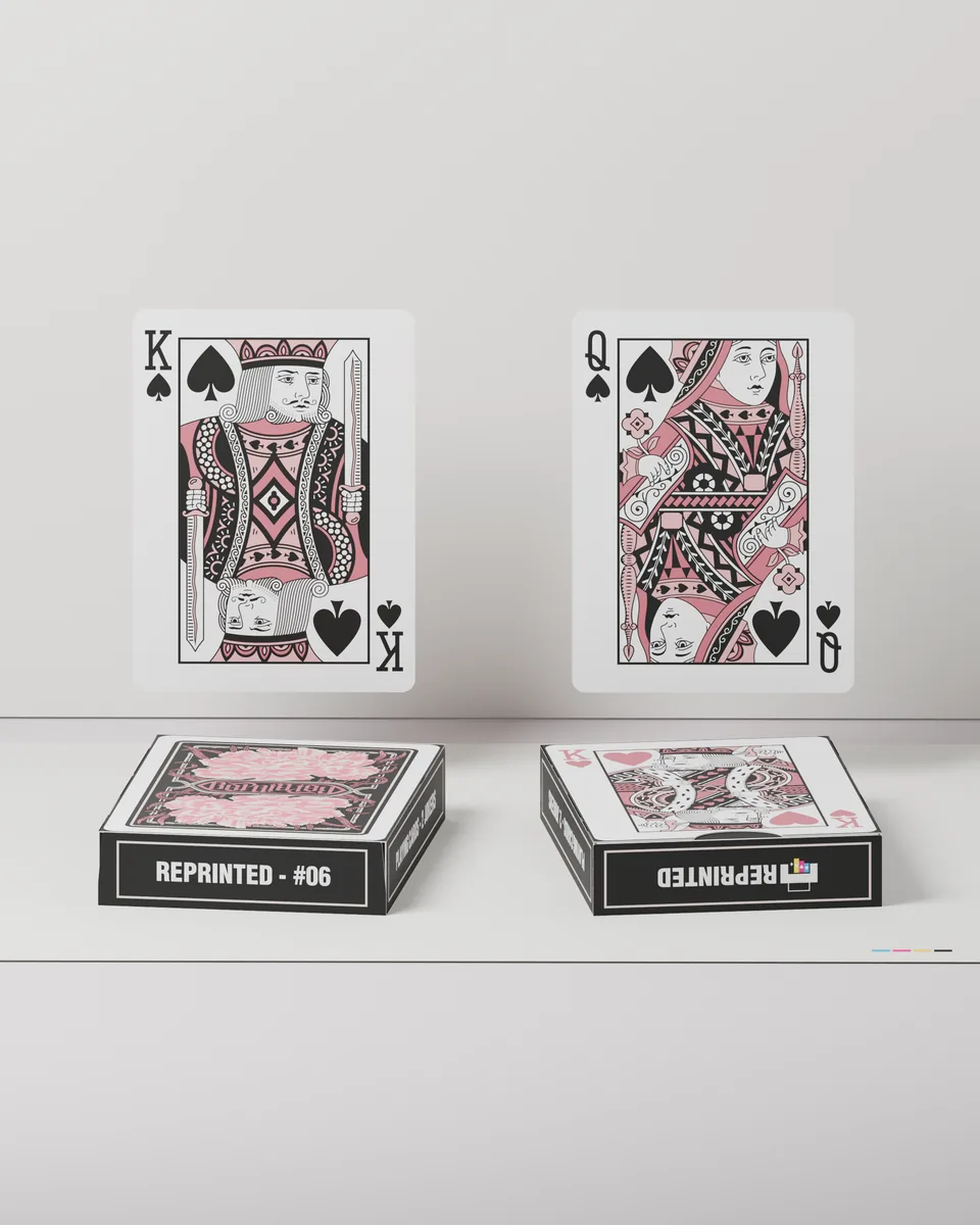 The king and queen of spades from REPRINTED #06 standing above two tuck cases